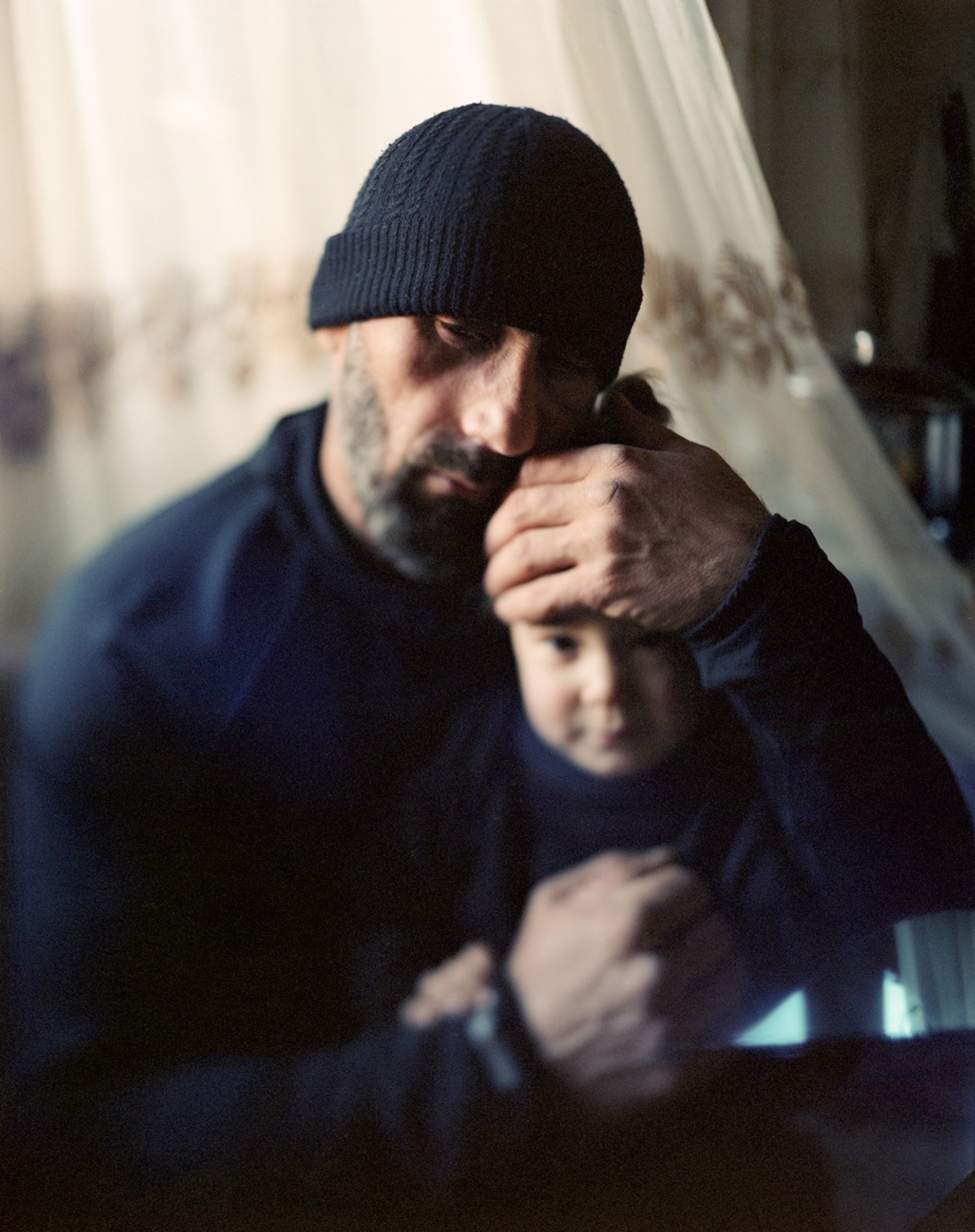 A man holding a child close in a layered interior portrait — Pankisi Valley