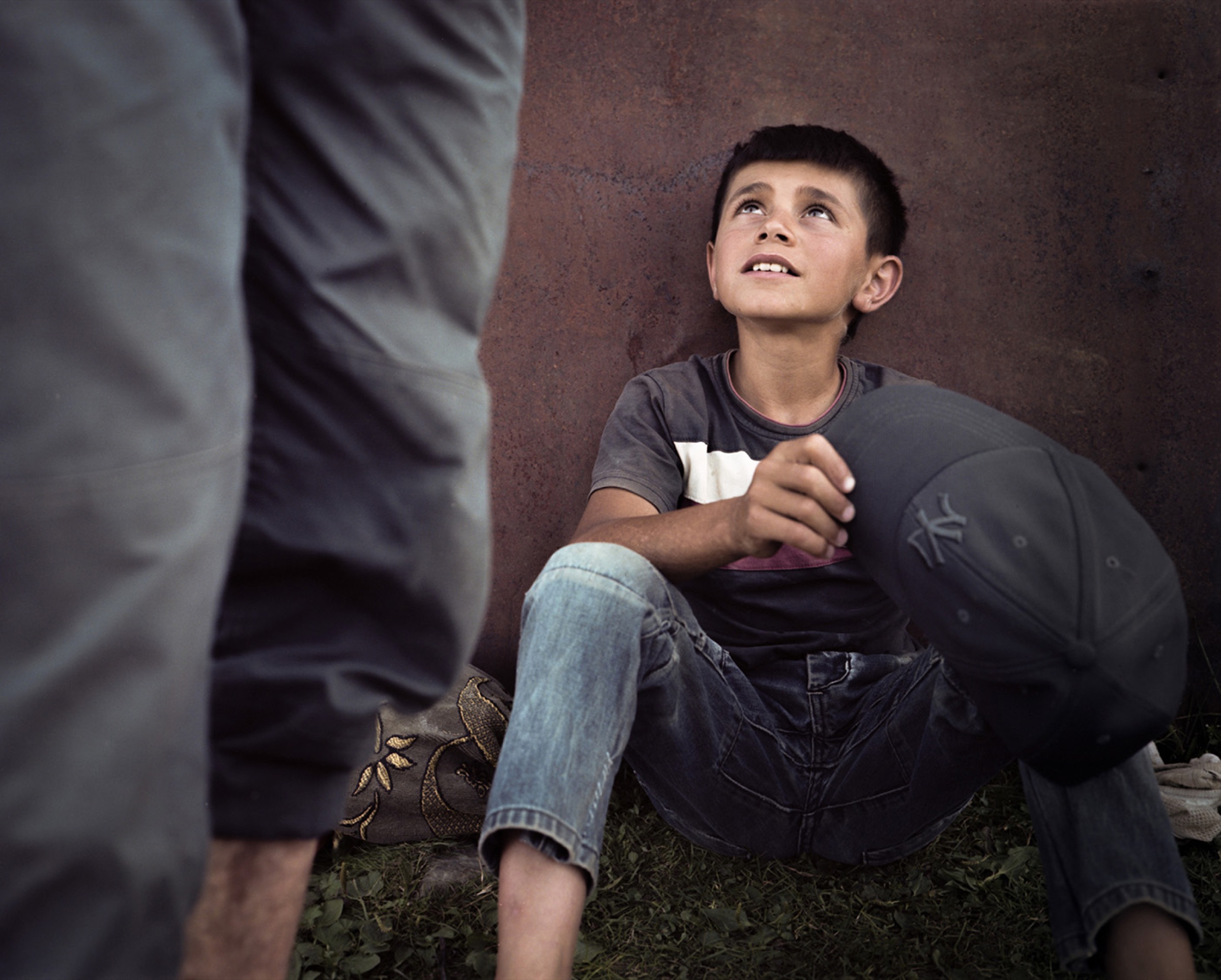 Boy sitting against a dark wall, gazing upward toward a man standing at the edge of the frame — Pankisi Valley
