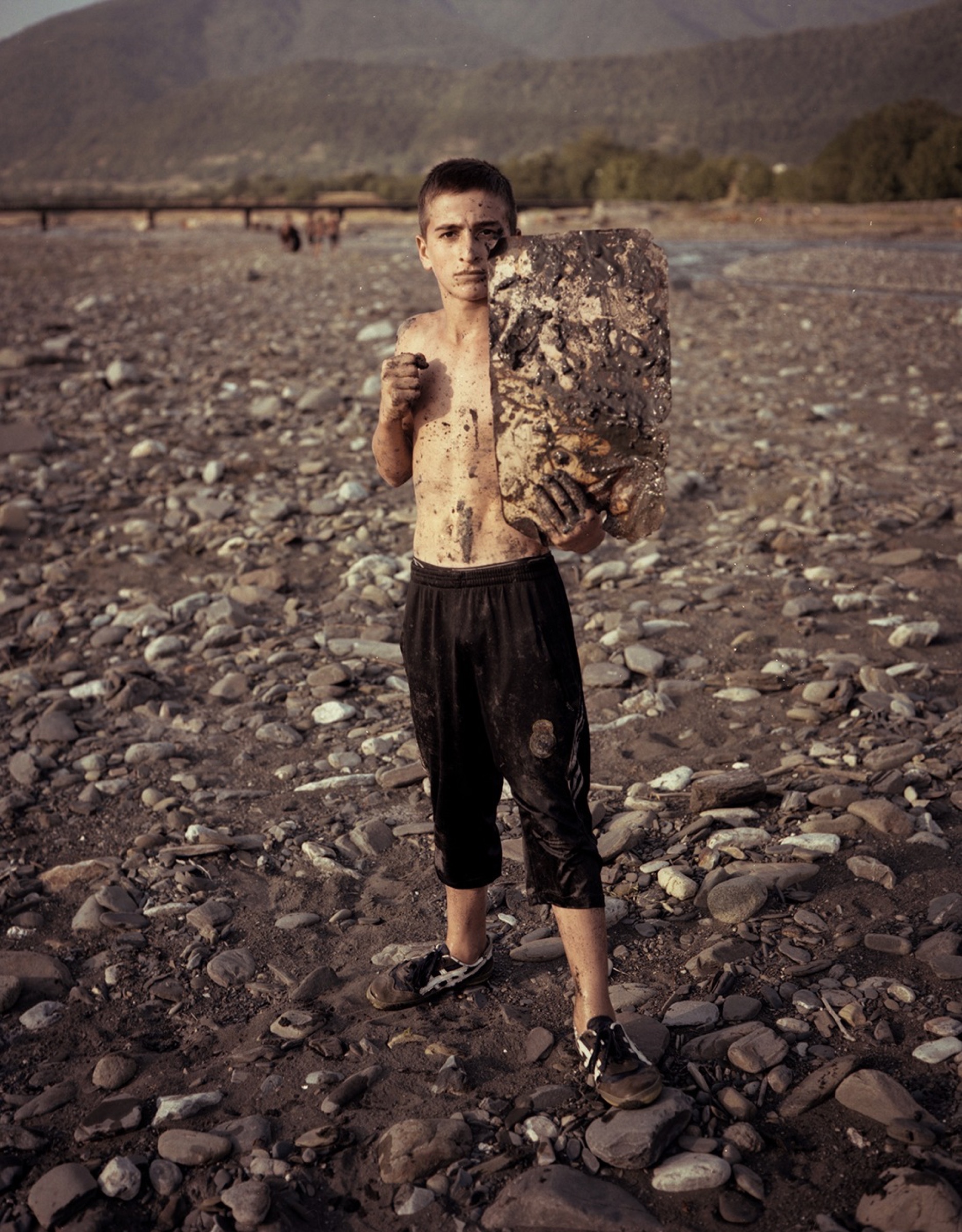 Young man standing on a rocky riverbed, holding a large stone — Pankisi Valley