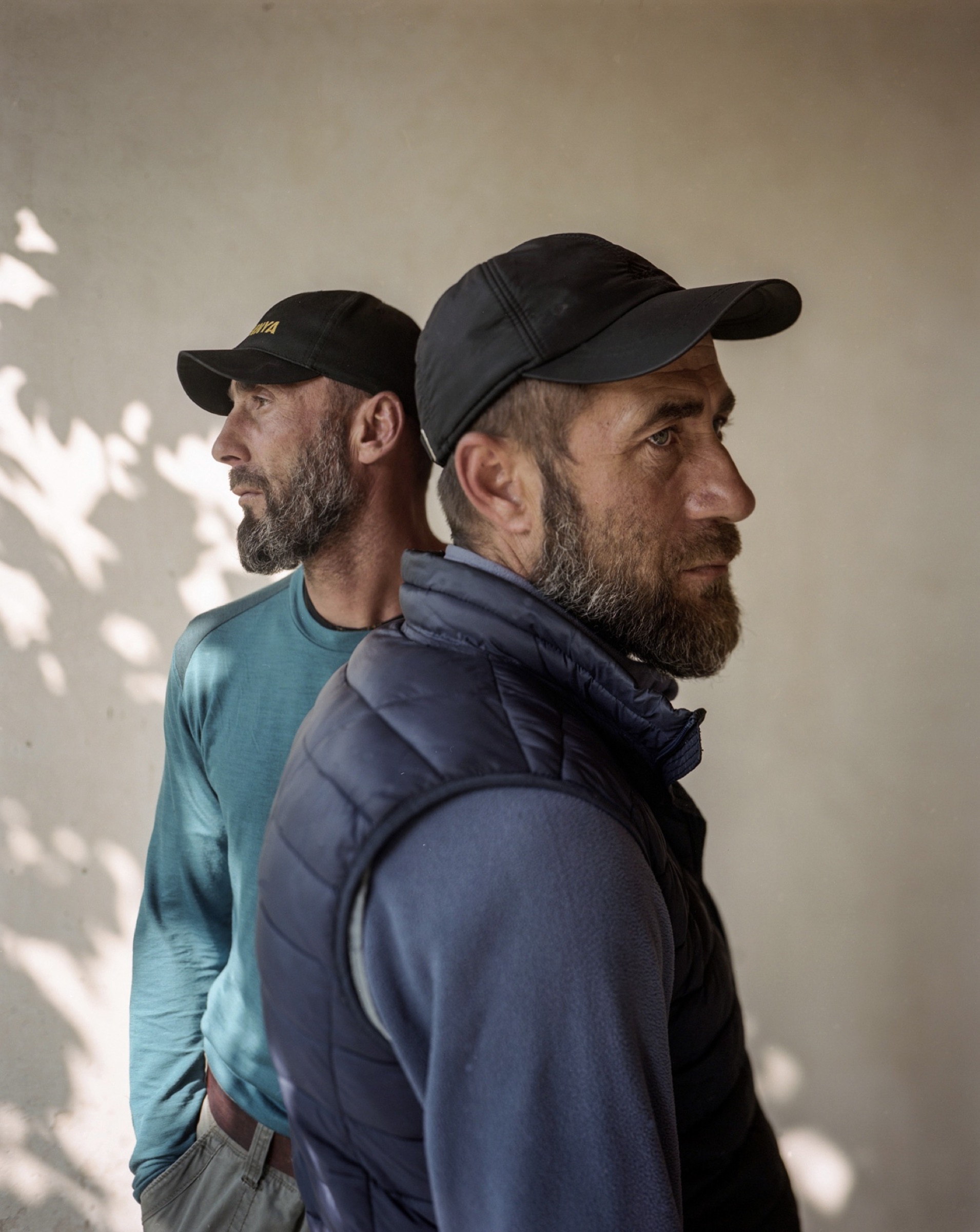 Two men photographed in profile against a white wall with dappled shadow — Pankisi Valley