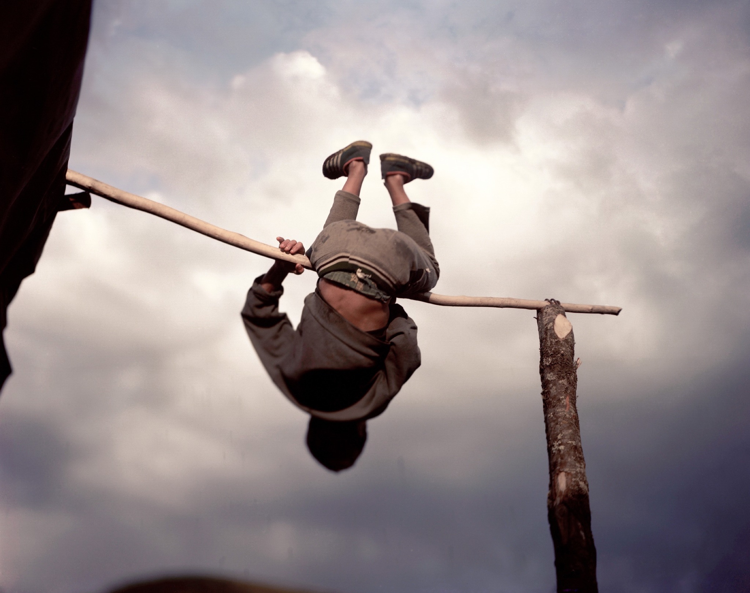 Boy hanging upside down from a wooden bar against a vast cloudy sky — Pankisi Valley