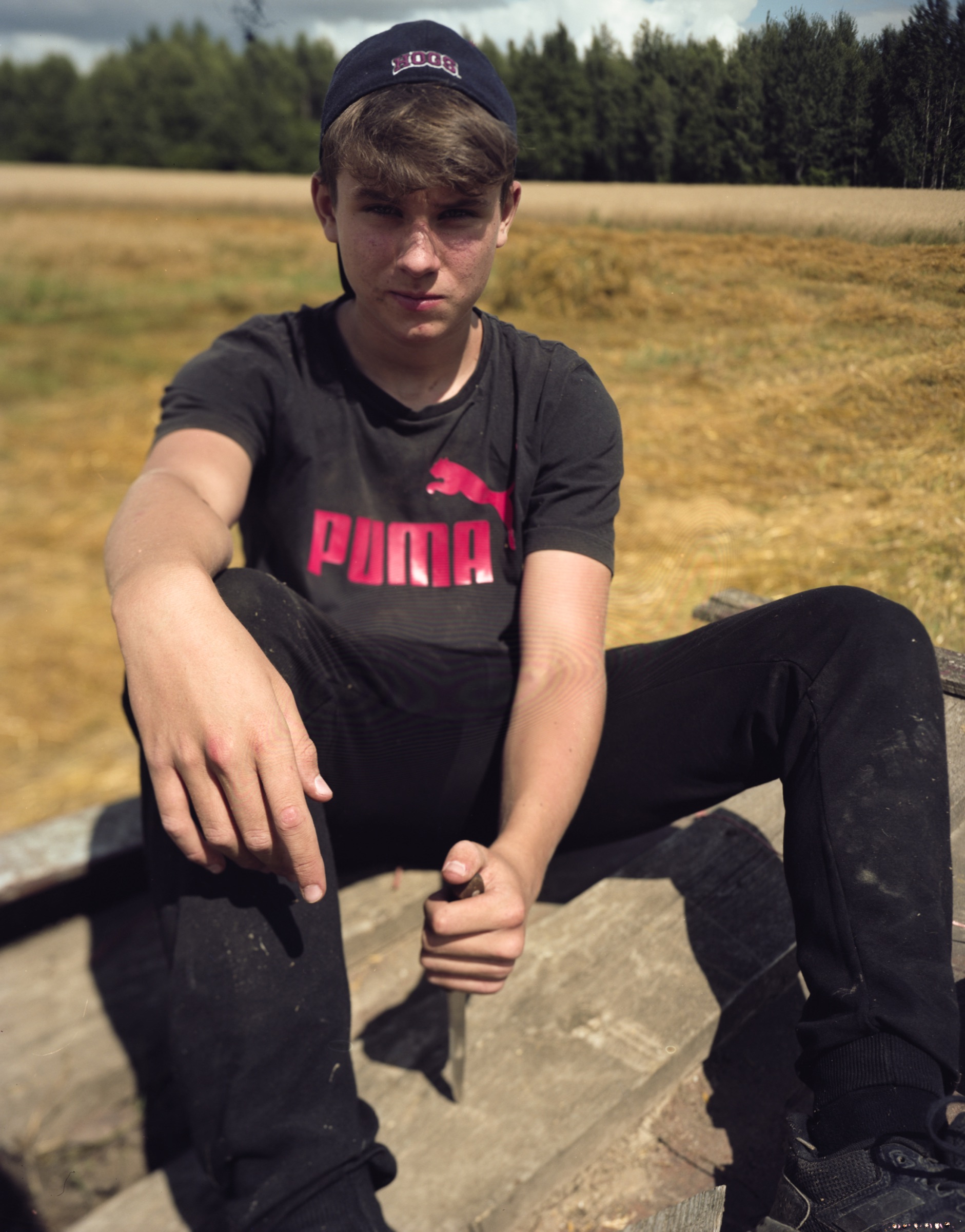 Young man in a Puma t-shirt sitting on wooden steps, looking directly at camera — Podlasie