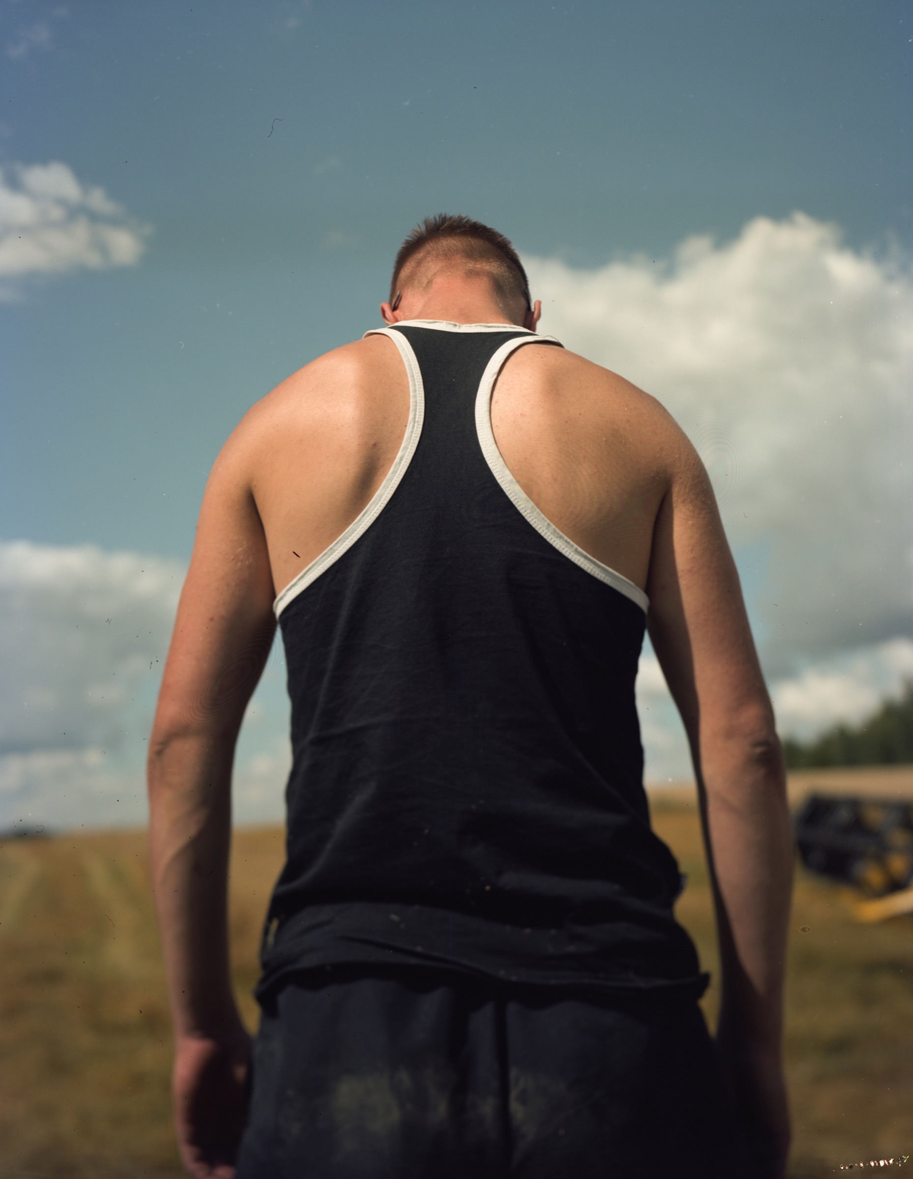 Young man from behind in a tank top, field and sky stretching behind him — Podlasie