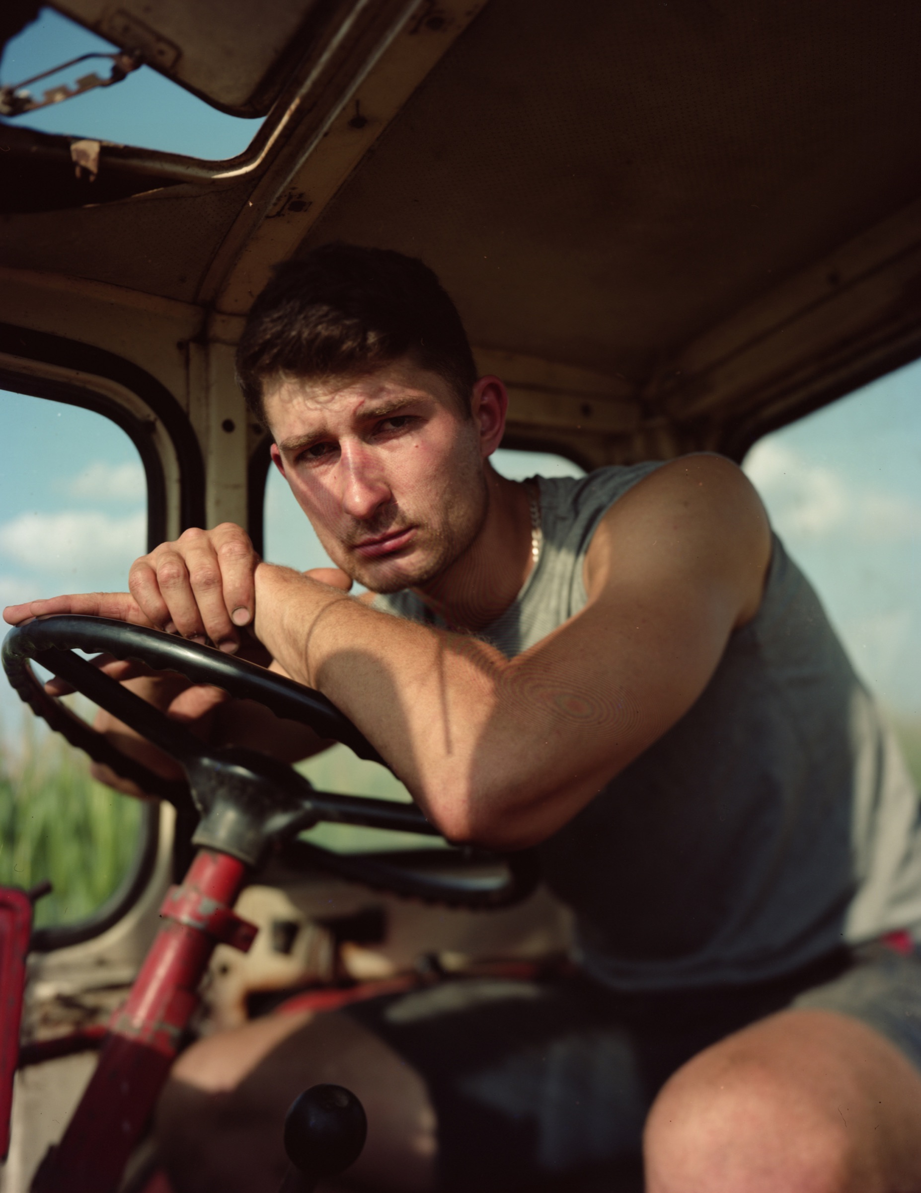 Young man leaning on the steering wheel inside an old tractor, looking at camera — Podlasie