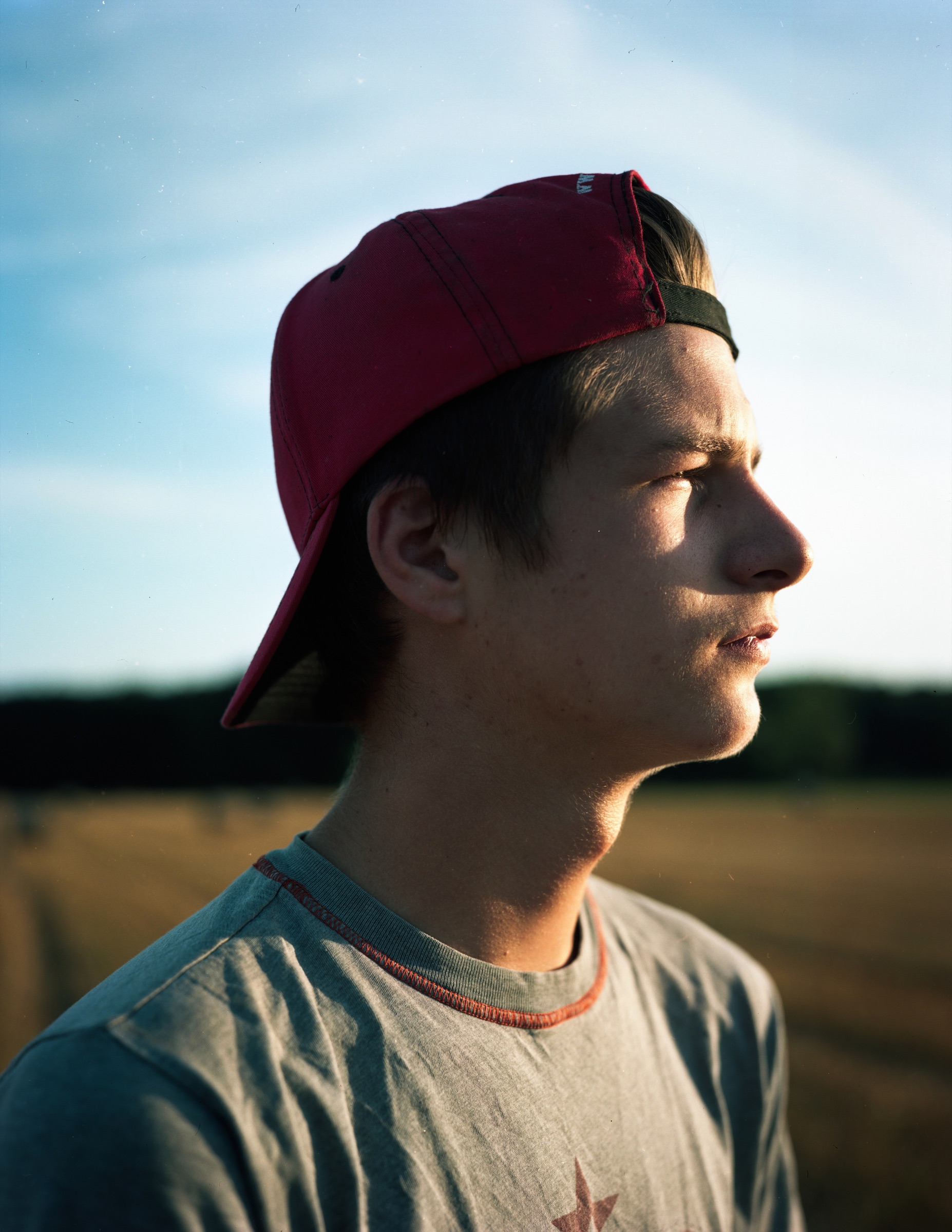 Young man in a red cap, profile portrait against a golden-hour field — Podlasie