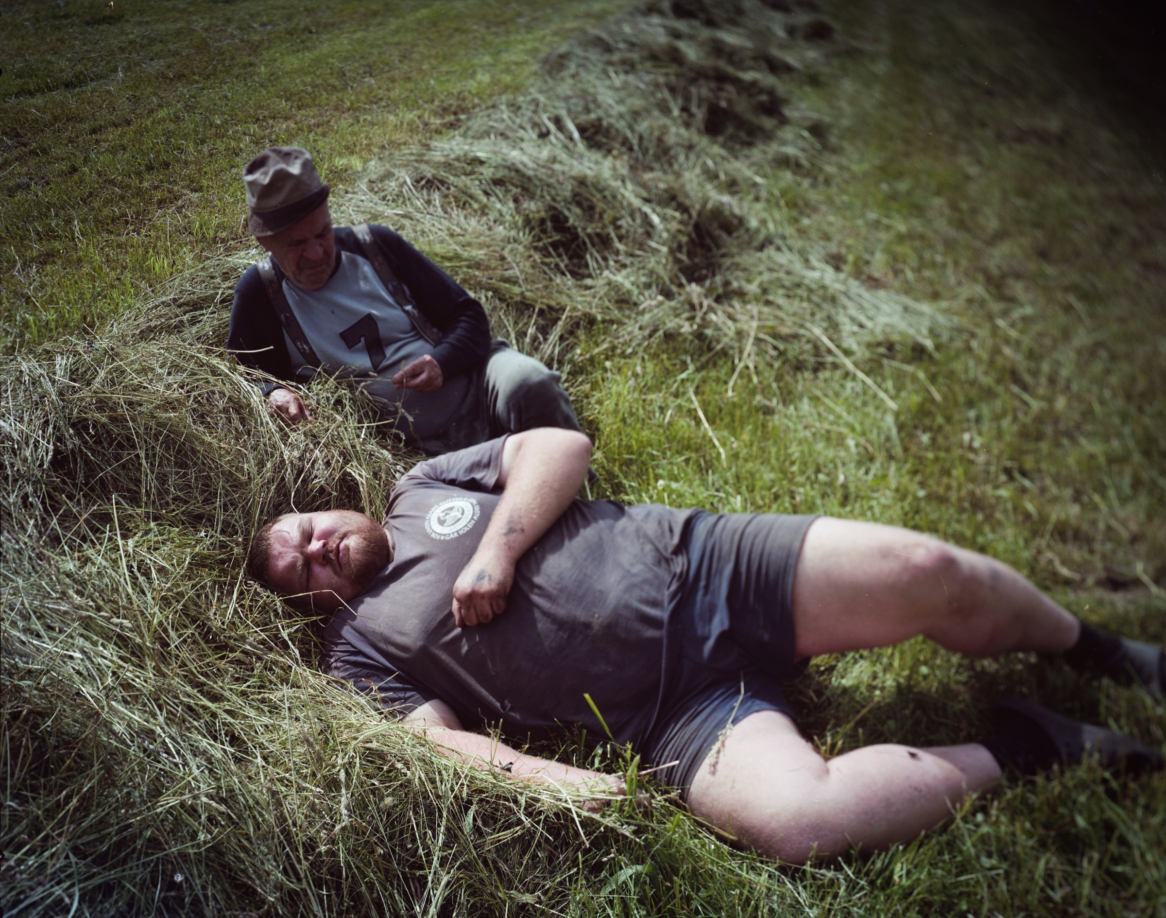 Young man lying on fresh hay, older man sitting beside him resting — Podlasie