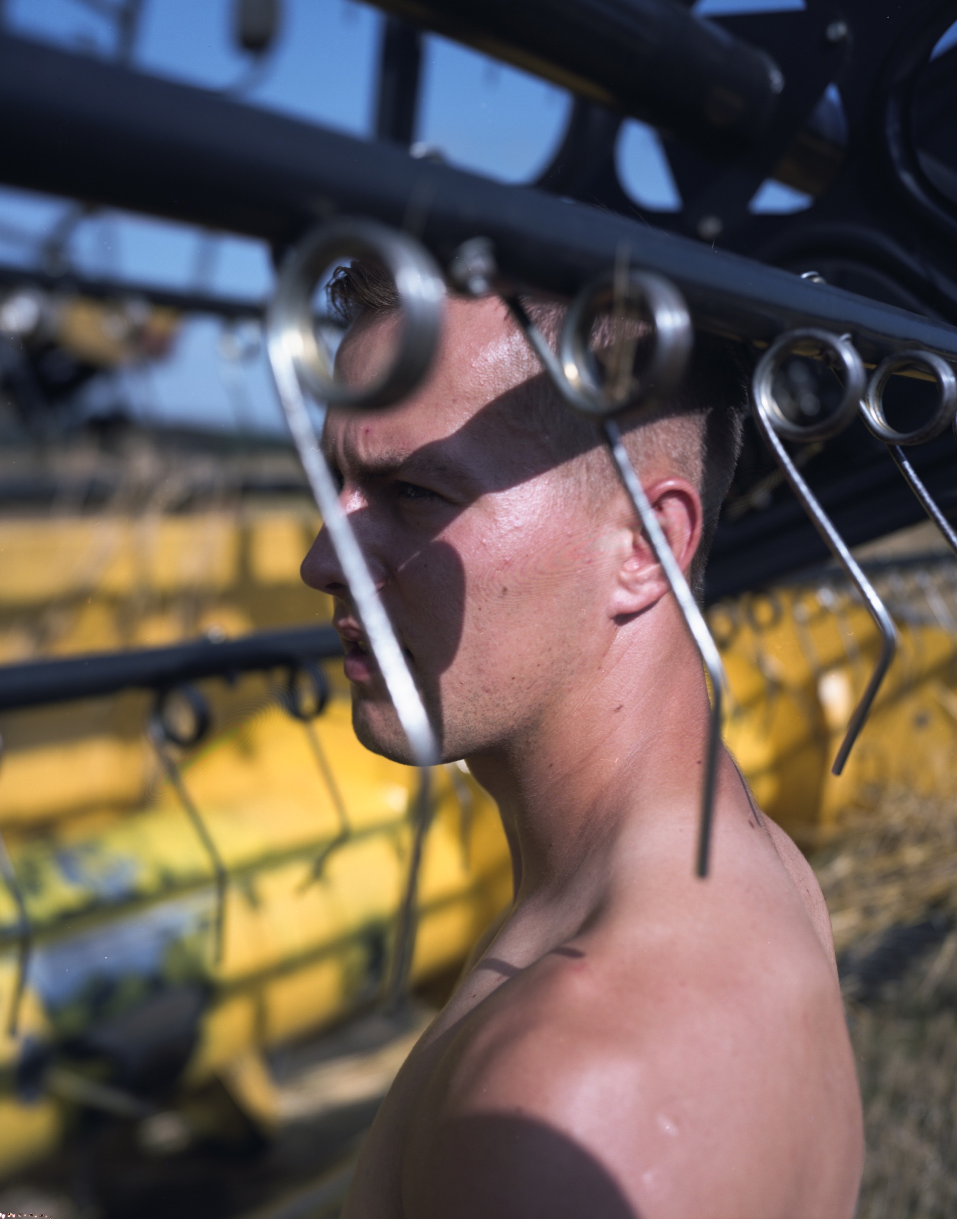 Shirtless young man in profile, mechanical arms of a yellow combine harvester framing his face — Podlasie
