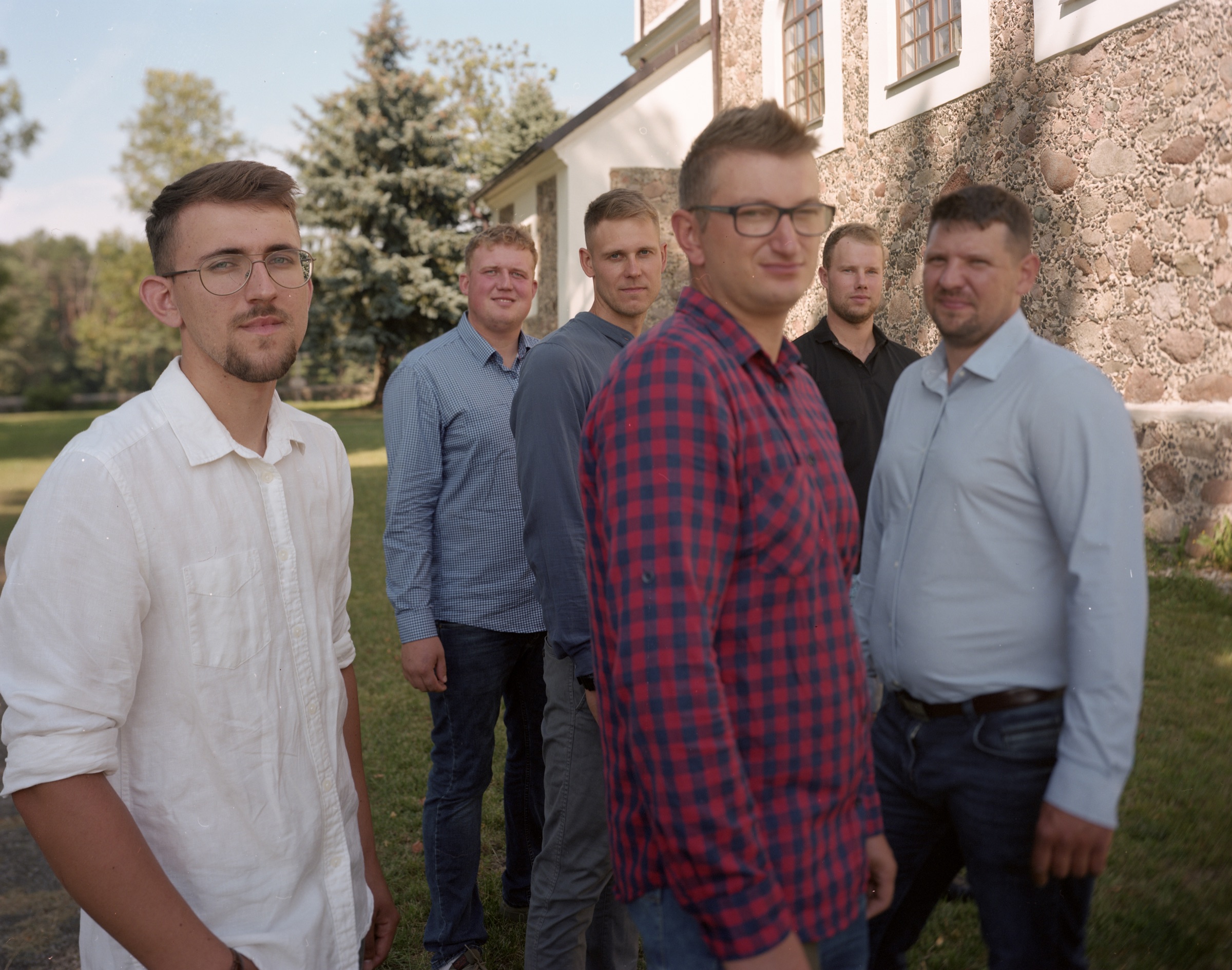 Group of young men in dress shirts gathered near a stone church building — Podlasie