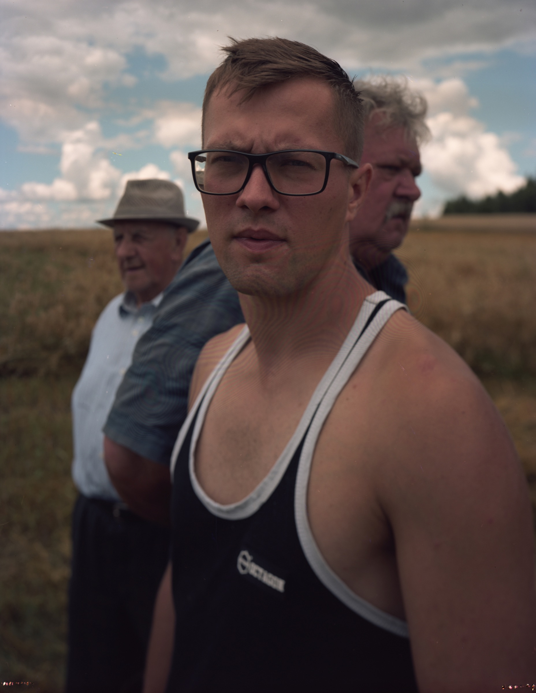 Young man in the foreground, two older men behind him — field and open sky — Podlasie