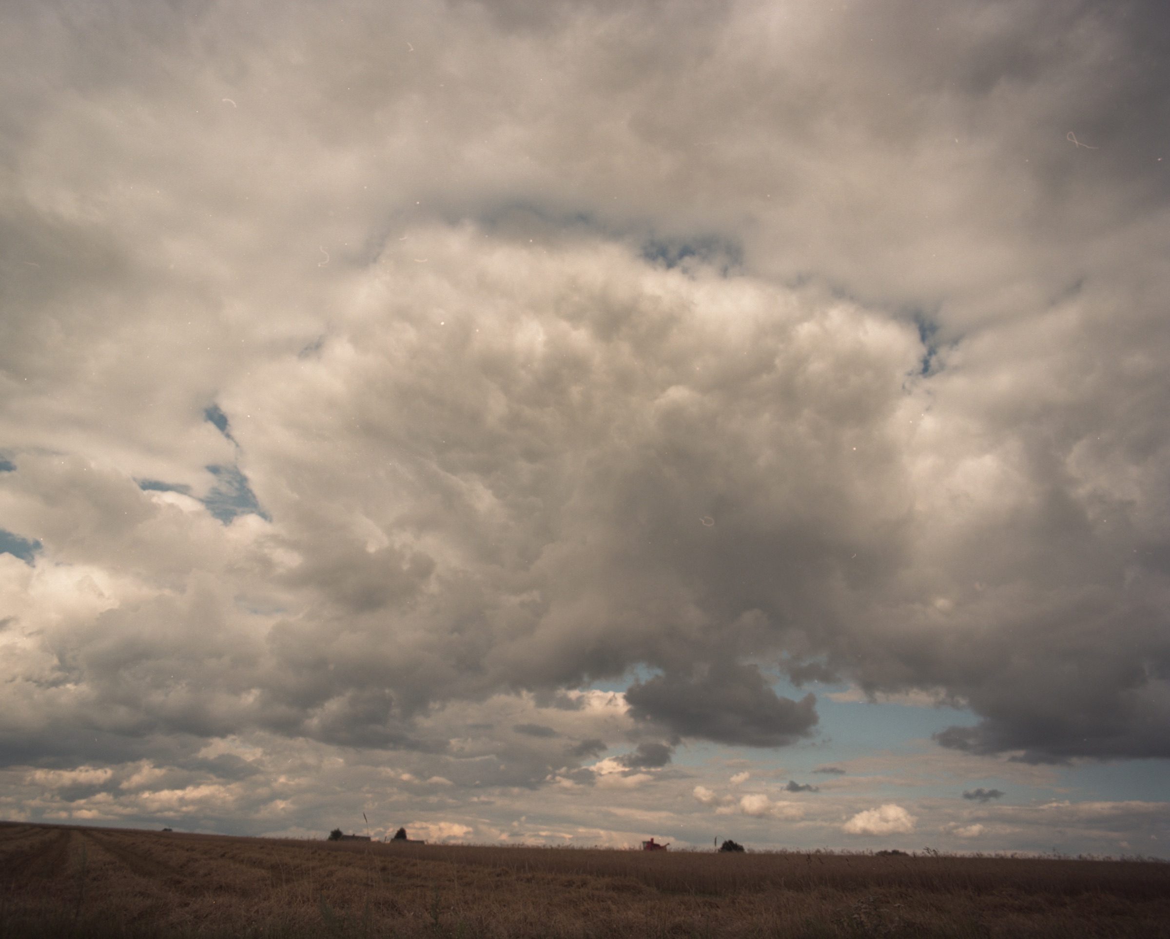 Vast storm sky over open Podlasie fields, a combine barely visible on the horizon